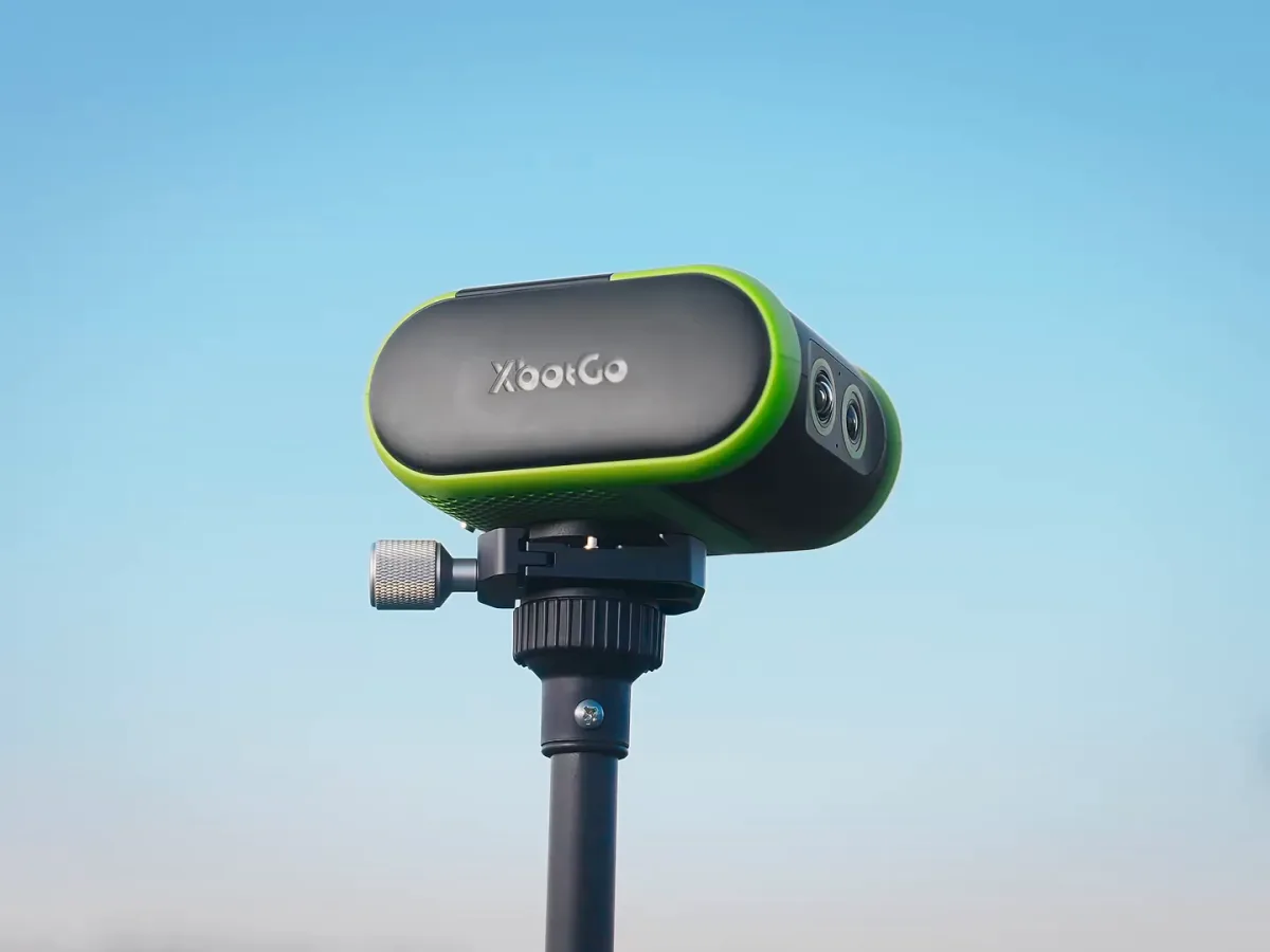 XbotGo Falcon, a black camera with a lime-green edge and two lenses, on a tripod against the sky