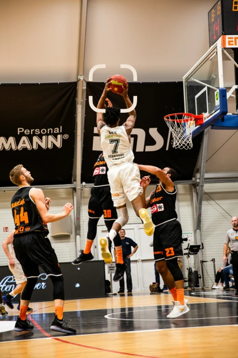 A player rises above two defenders to finish at the rim.